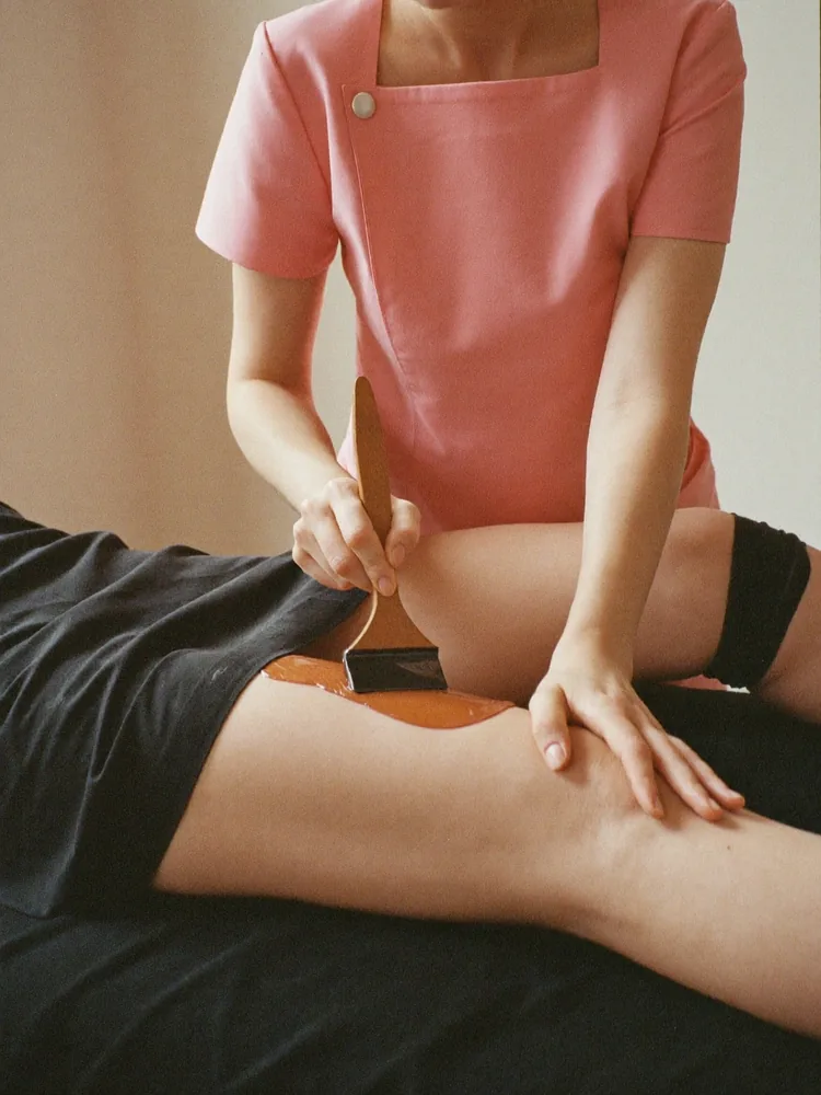 Therapist waxing a client's calf, the client wearing leggings