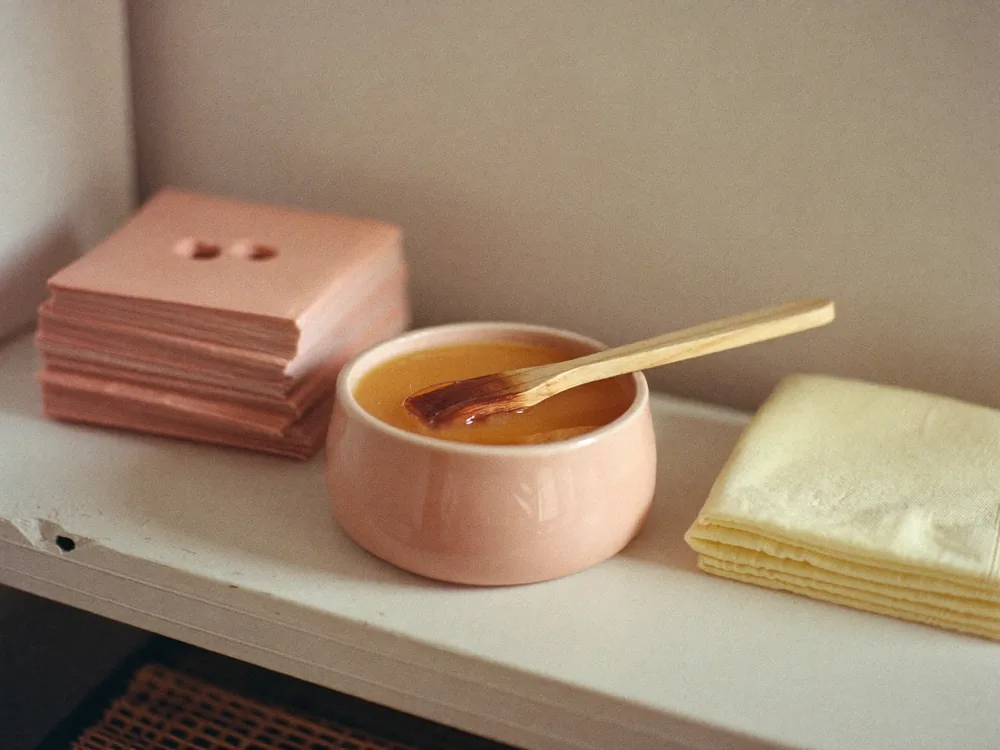 A pot of warm wax, spatula and folded strips on a shelf